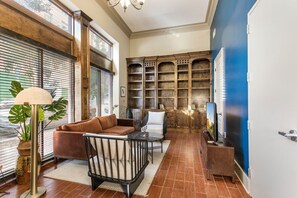 A cozy living room with a brown leather sofa, a black chair, a small round table, and a floor lamp. There is a bookshelf with multiple shelves and a television on a stand.