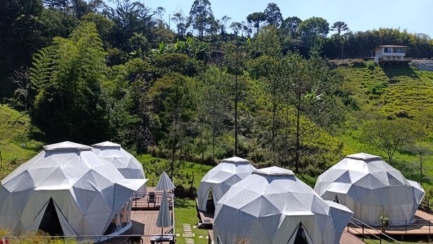 Una serie de estructuras de cúpulas geodésicas con terrazas de madera y mobiliario exterior, rodeadas de exuberante vegetación y un paisaje montañoso.