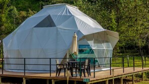 Una estructura en forma de cúpula geodésica con terraza de madera y zona de estar al aire libre.
