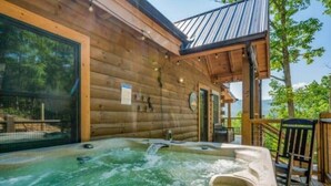 Une cabane en bois avec un jacuzzi sur une terrasse, donnant sur une étendue d’eau.