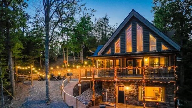 Un chalet à deux étages avec une façade en pierre, une véranda et une guirlande de lumières.