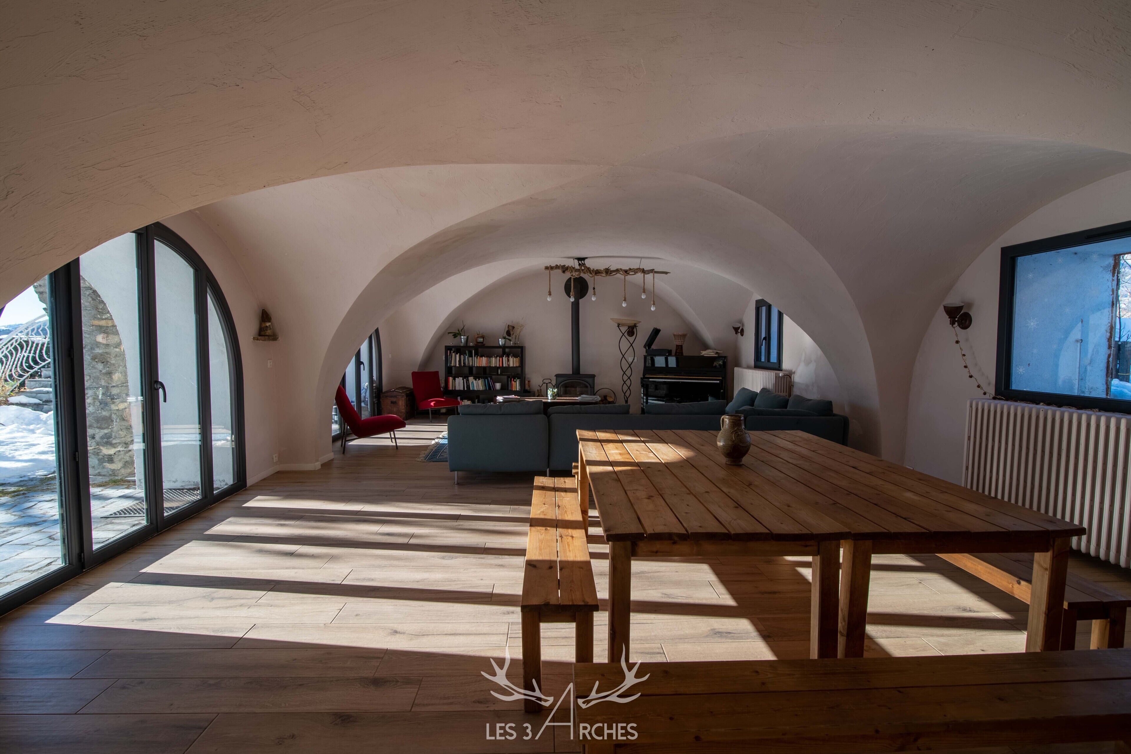An interior with arched ceilings, a wooden dining table, and a cozy seating area with sofas and a bookshelf.