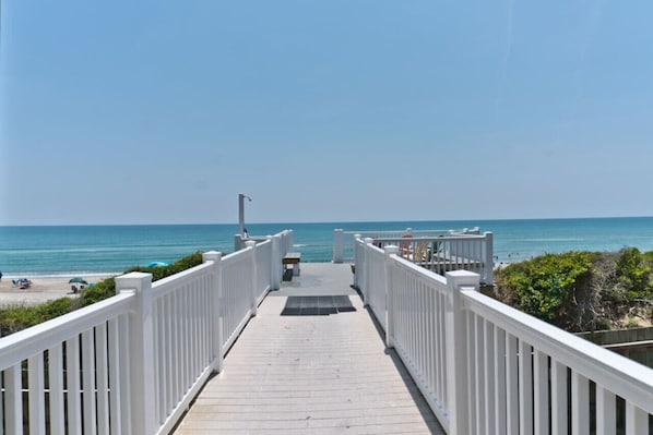 A wooden boardwalk leading to a beach with a clear view of the ocean.