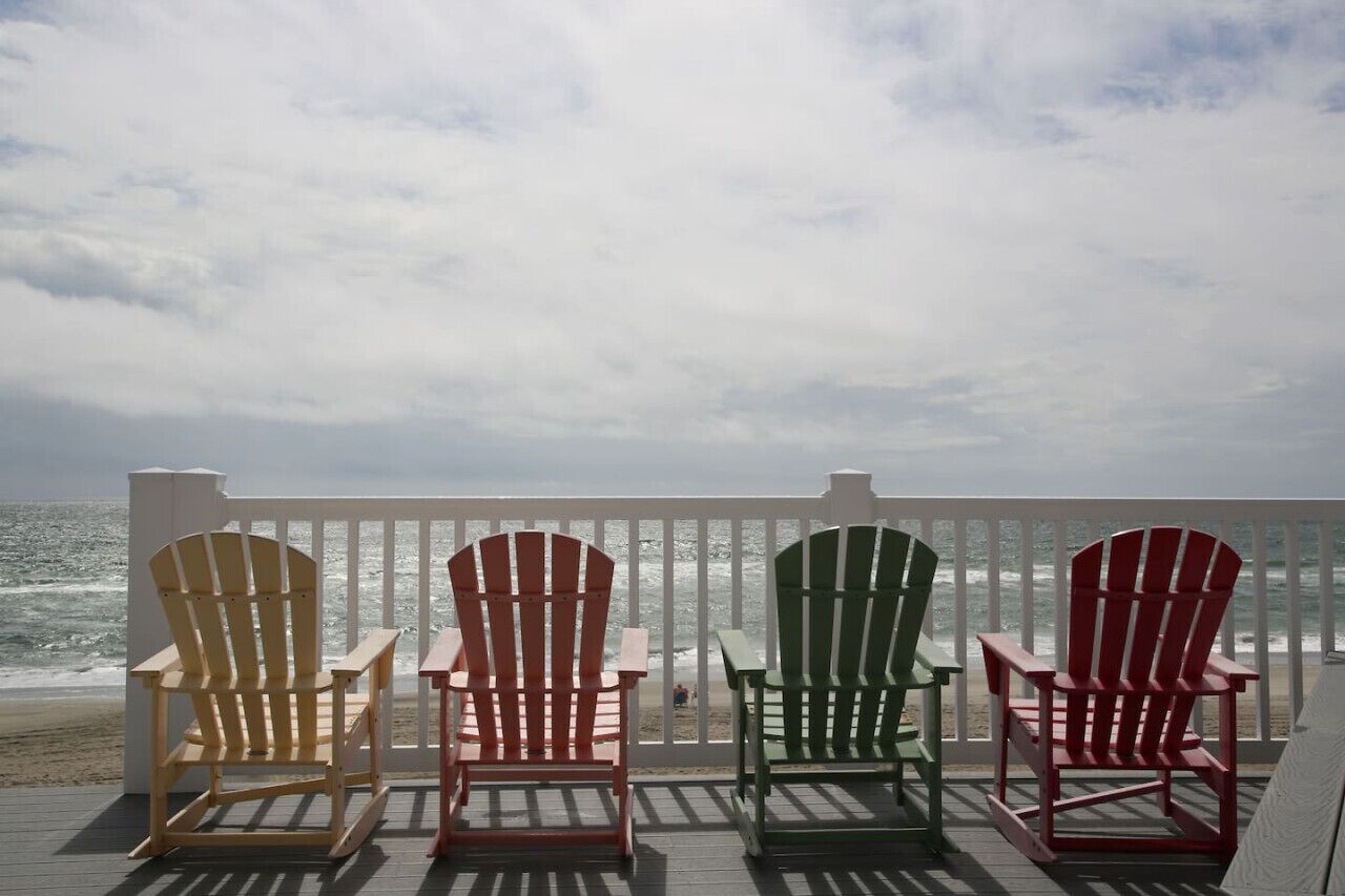 A deck with four Adirondack chairs facing the ocean.