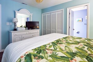 Une chambre à coucher avec un lit, une commode, un téléviseur et une porte.