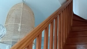 Una escalera de madera con barandilla, que lleva a una habitación con ventilador de techo y ventana.
