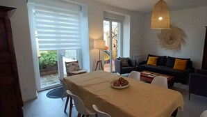 Un comedor con una mesa lista para dos, un sofá con cojines amarillos y una lámpara colgante.