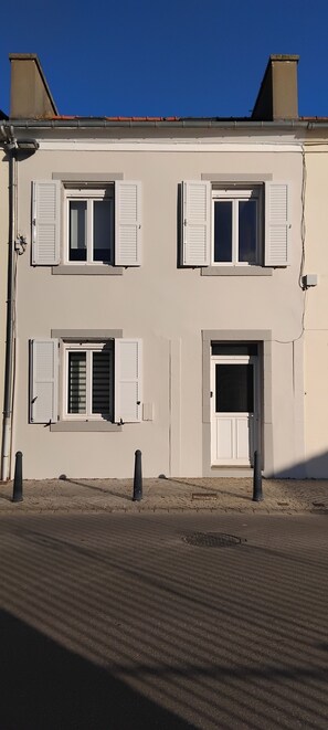 A two-story building with white shutters on the windows, a door, and a small porch area. - maison vue mer au bourg du Conquet (Le Conquet)