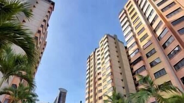 Um edifício residencial alto com várias varandas, rodeado por palmeiras e um céu claro.