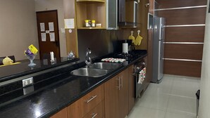 Cozinha moderna com armários de madeira, bancada preta, eletrodomésticos de aço inoxidável e forno embutido.