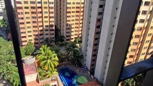 Um edifício alto com várias varandas e uma pequena área de piscina com palmeiras.