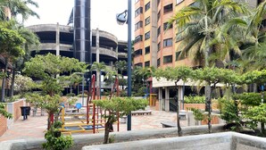 Pátio com parquinho, palmeiras e um estacionamento de vários níveis ao fundo.