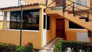 Un edificio de dos pisos con fachada amarilla, puerta de madera y escalera con barandillas negras.