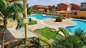 Zona de piscina con un pabellón, palmeras y un edificio de techo rojo.