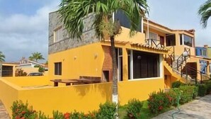 Un edificio amarillo con balcón, escaleras y una palmera.