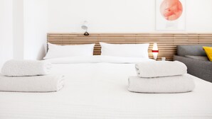 Una habitación de hotel con una cama bien hecha, una mesita de noche con una lámpara, y un sofá con un cojín.