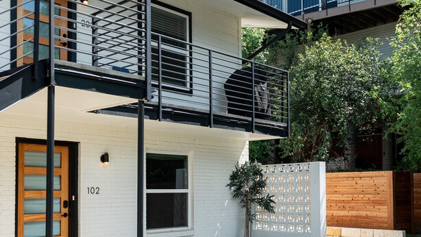 Een huis met twee verdiepingen, een balkon, een houten deur en het nummer '102' op de gevel.