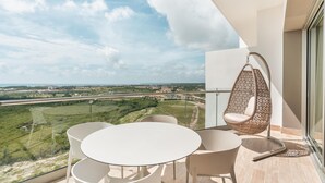 A balcony with a round table and chairs, a hanging chair, and a view of a green landscape and distant road. - 7 Mares D12 in Punta Cana (Punta Cana)