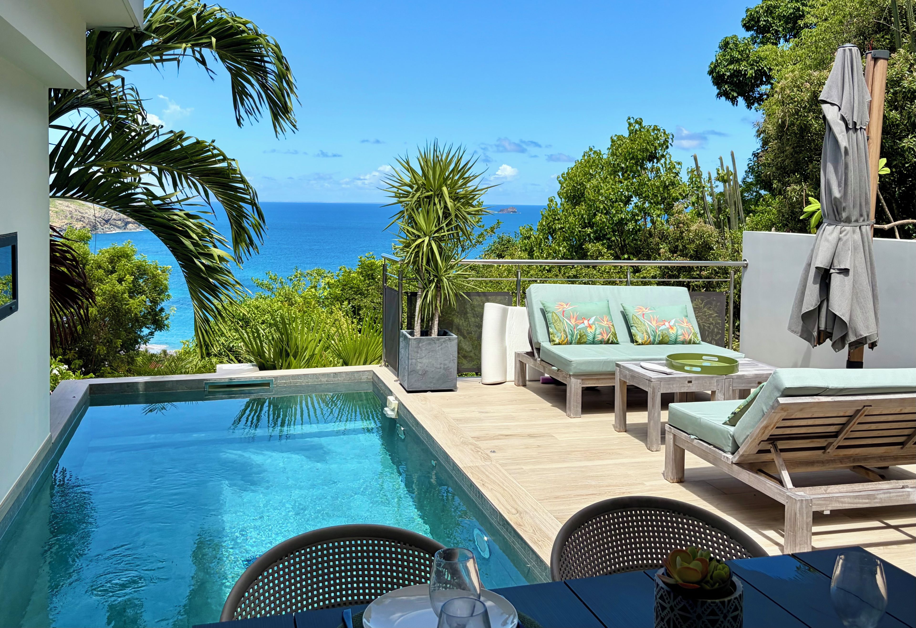A poolside area with a view of the ocean, lounge chairs, and a table with a glass.