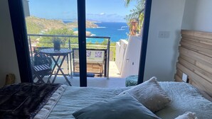 Un dormitorio con cama, almohadas y vista al océano a través de una puerta de vidrio.