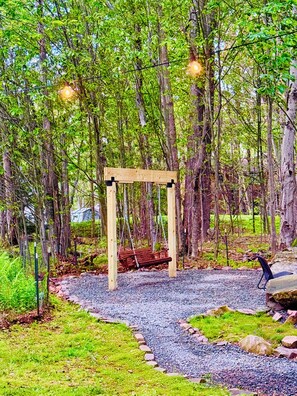 A wooden swing set in a wooded area with a gravel path and a metal bench. - Stylish 3 Bed Mtn Retreat with HOT TUB, KING SIZE BED & Resort Style Amenities.  (Tobyhanna)