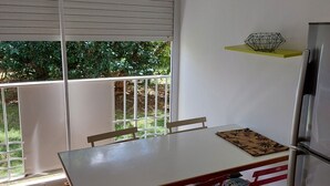 Uma área de refeições com mesa, cadeiras, geladeira e janela com persianas.