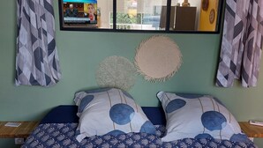 Quarto com cama, janela ampla, ventoinha no teto e painéis decorativos na parede.