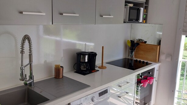 Uma cozinha moderna com armários brancos, forno embutido, micro-ondas, cafeteira e máquina de lavar roupa.
