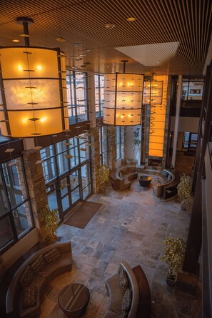 Een ruime lobby met een hoge plafond, grote ramen en moderne verlichtingsarmaturen.