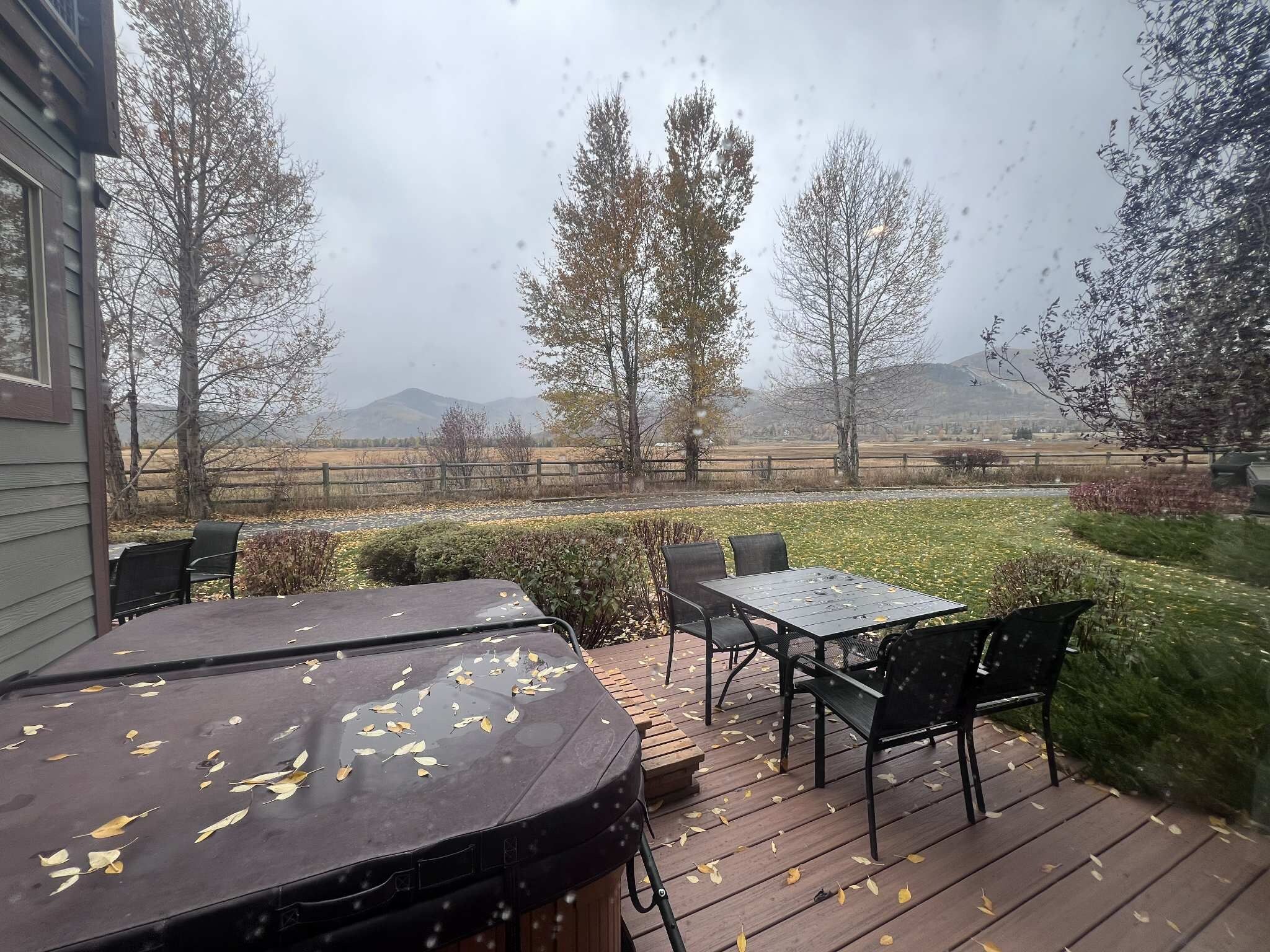 Une terrasse avec une table et des chaises, entourée d’une plateforme en bois et offrant une vue sur un champ et des arbres.