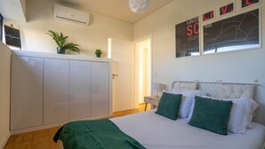 A bedroom with a bed, a wardrobe, a bedside table, and a wall with artwork. - Porto Heights by LovelyStay (Porto)