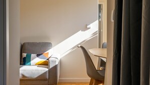 A room with a sofa and a desk, sunlight streaming through a window, and a door leading to another room. - Porto Heights by LovelyStay (Porto)