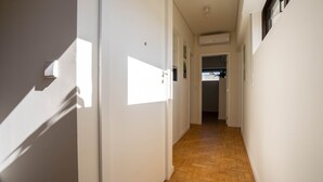 A narrow hallway with white walls and wooden flooring, leading to a room with a window and an air conditioning unit. - Porto Heights by LovelyStay (Porto)