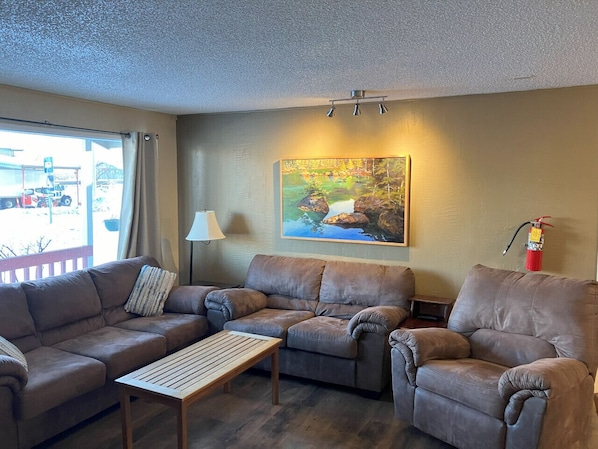 A living room with two sofas, a wooden coffee table, a lamp, a painting, and a fire extinguisher.