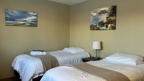Habitación de hotel con dos camas, una mesita de noche con lámpara y dos cuadros en las paredes.