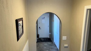 A hallway with an EXIT sign, a framed picture on the wall, and a door at the end. - Halibut House Unit 2 (Seward)