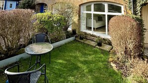 A stone building with a tiled roof, a small garden with a table and chairs, and a large window. - Captivating 2-bed Cottage in Kingsbarns (St. Andrews)