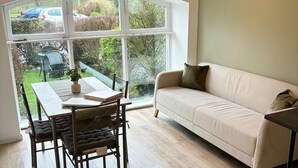 A cozy room with a large window, a dining table, and a sofa. - Captivating 2-bed Cottage in Kingsbarns (St. Andrews)