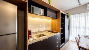 Una cocina moderna con un refrigerador de acero inoxidable, un microondas integrado y un lavamanos con grifo. Hay una mesa de comedor con sillas y una planta en la encimera.