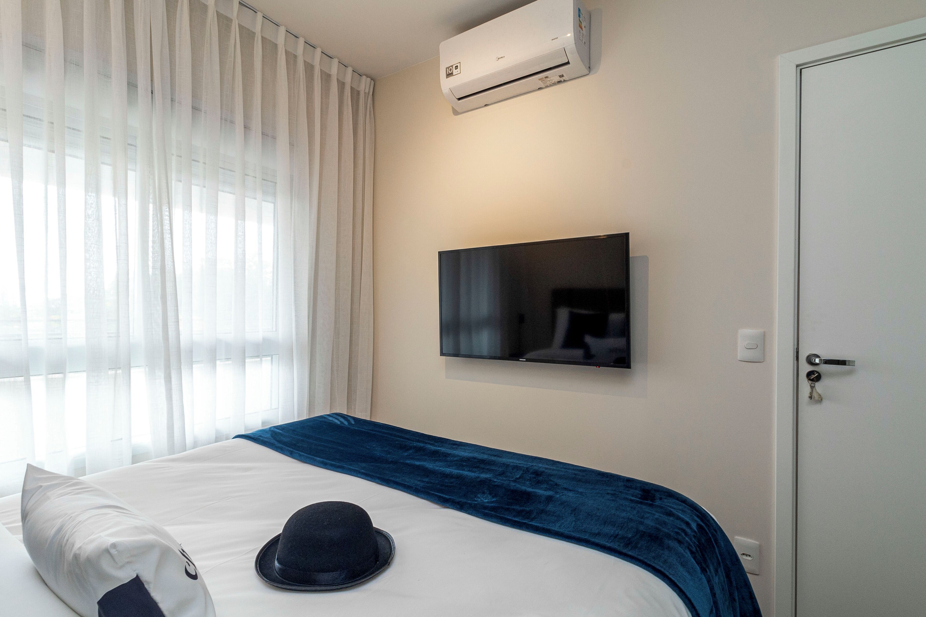 A hotel room with a bed, a flat-screen TV mounted on the wall, and a door with a key lock.