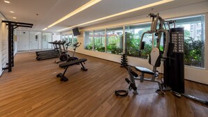 Un gimnasio moderno con piso de madera, diversos equipos de ejercicio y amplias ventanas con vistas a zonas verdes.