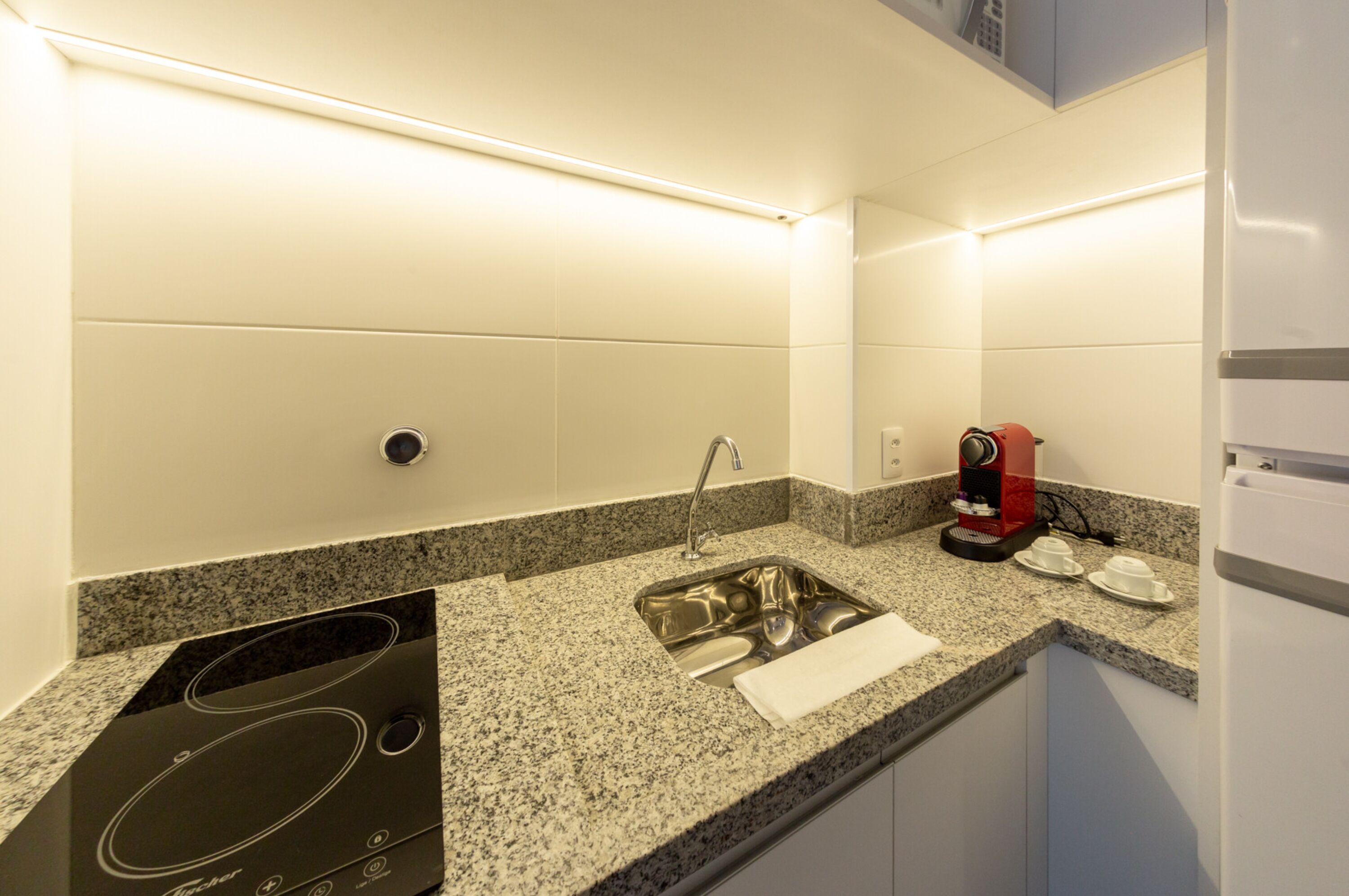 Una cocina con encimera de granito, pileta de acero inoxidable y cafetera.