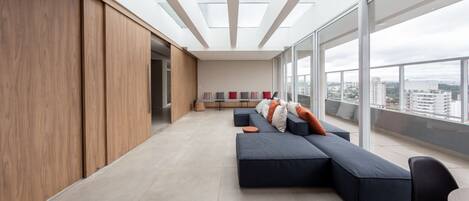A modern living room with a large sectional sofa, a dining area, and a view of the city through large windows.
