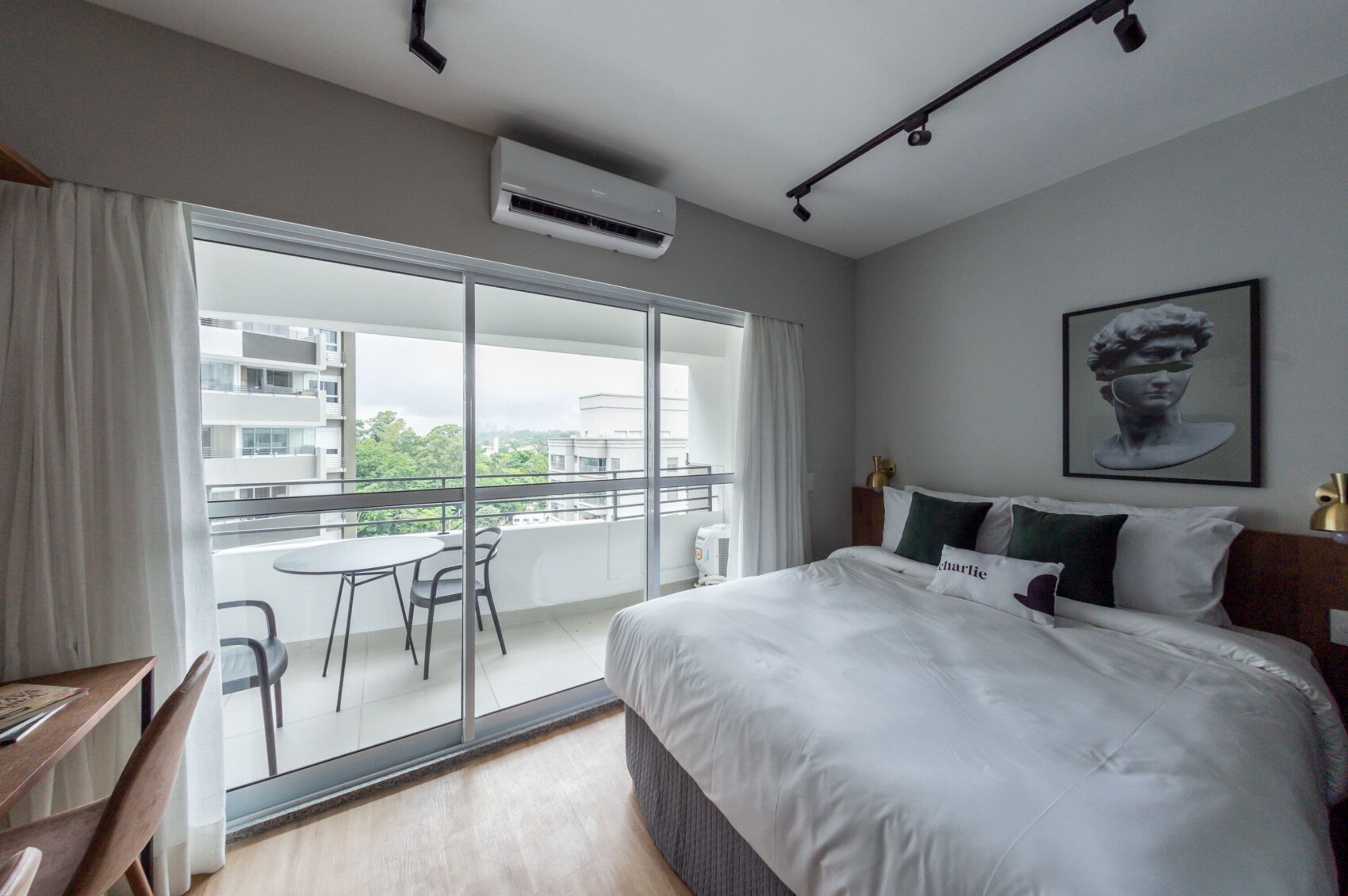Habitación de hotel con una cama grande, un balcón con mesa y sillas, y vistas a la ciudad.