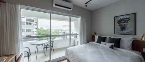 Ein Hotelzimmer mit einem großen Bett, einem Balkon mit Tisch und Stühlen sowie Blick auf die Stadt.