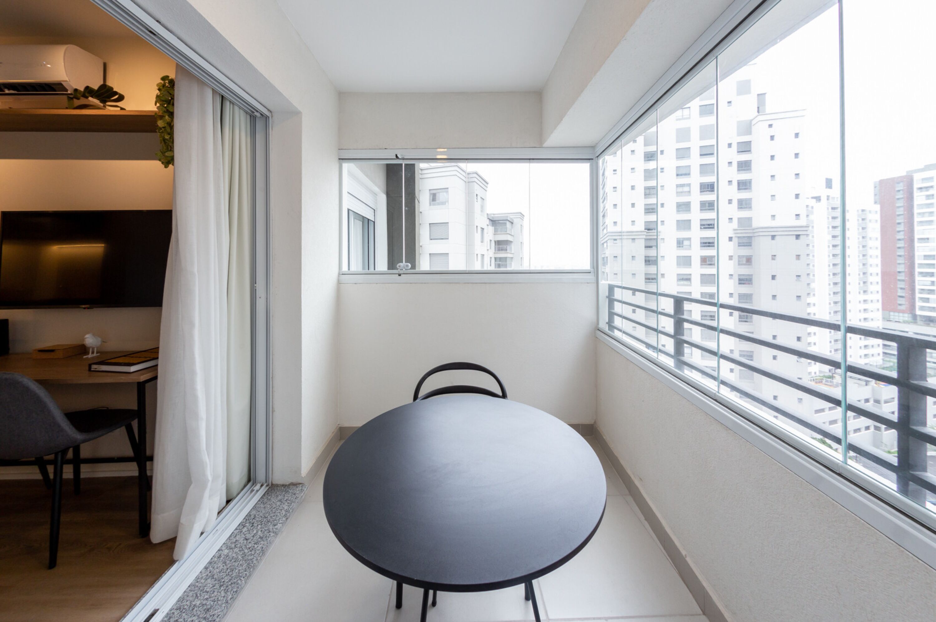 A small balcony with a round table and chairs, a TV, and a window with a city view.