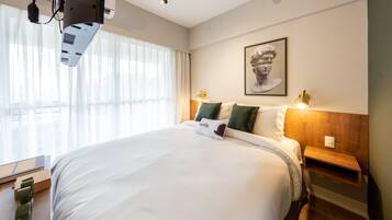 Una habitación de hotel con una cama grande, una mesita de noche de madera, un estante en la pared y una obra de arte enmarcada sobre la cama.