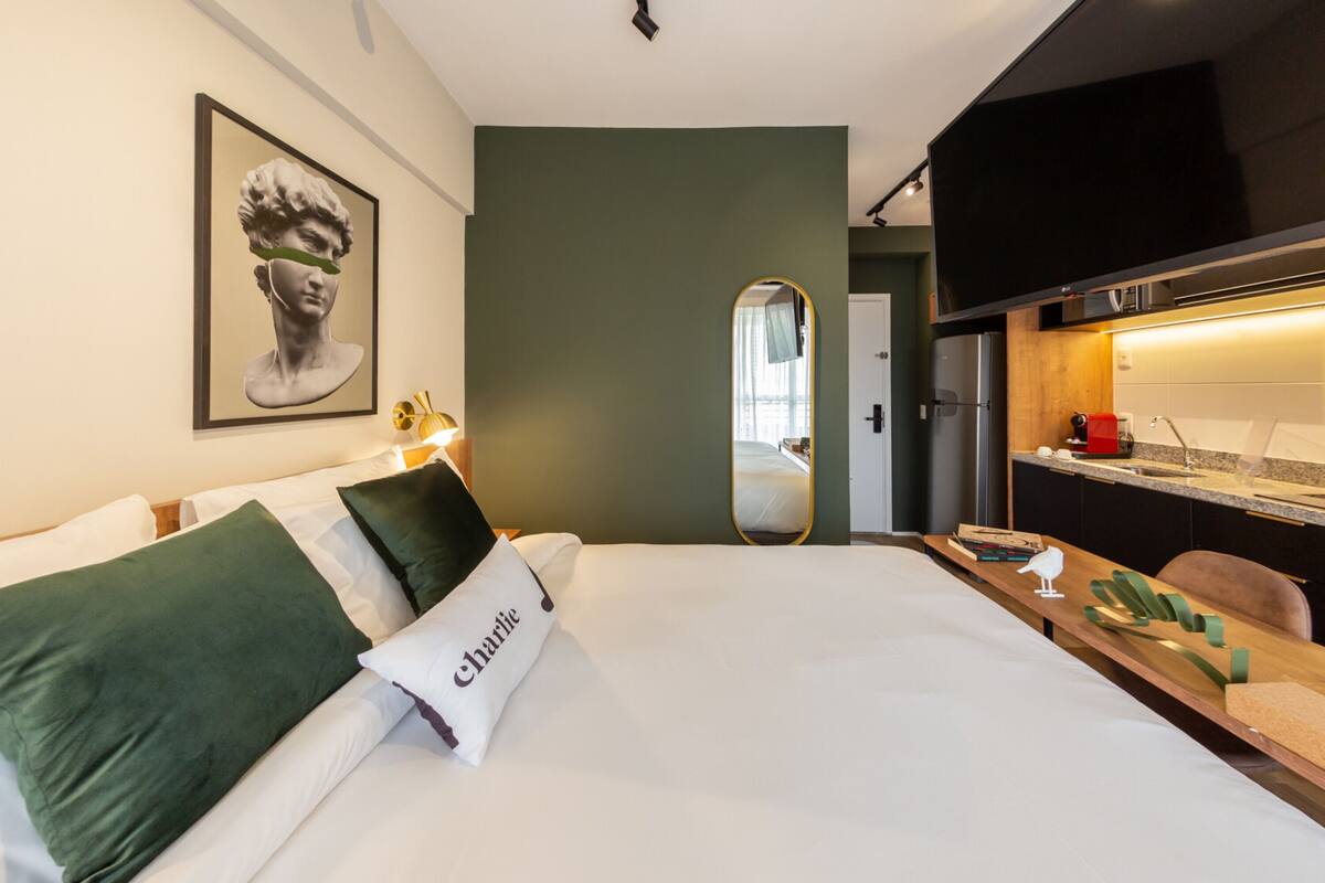 A hotel room with a bed, a desk, a mirror, and a kitchenette.