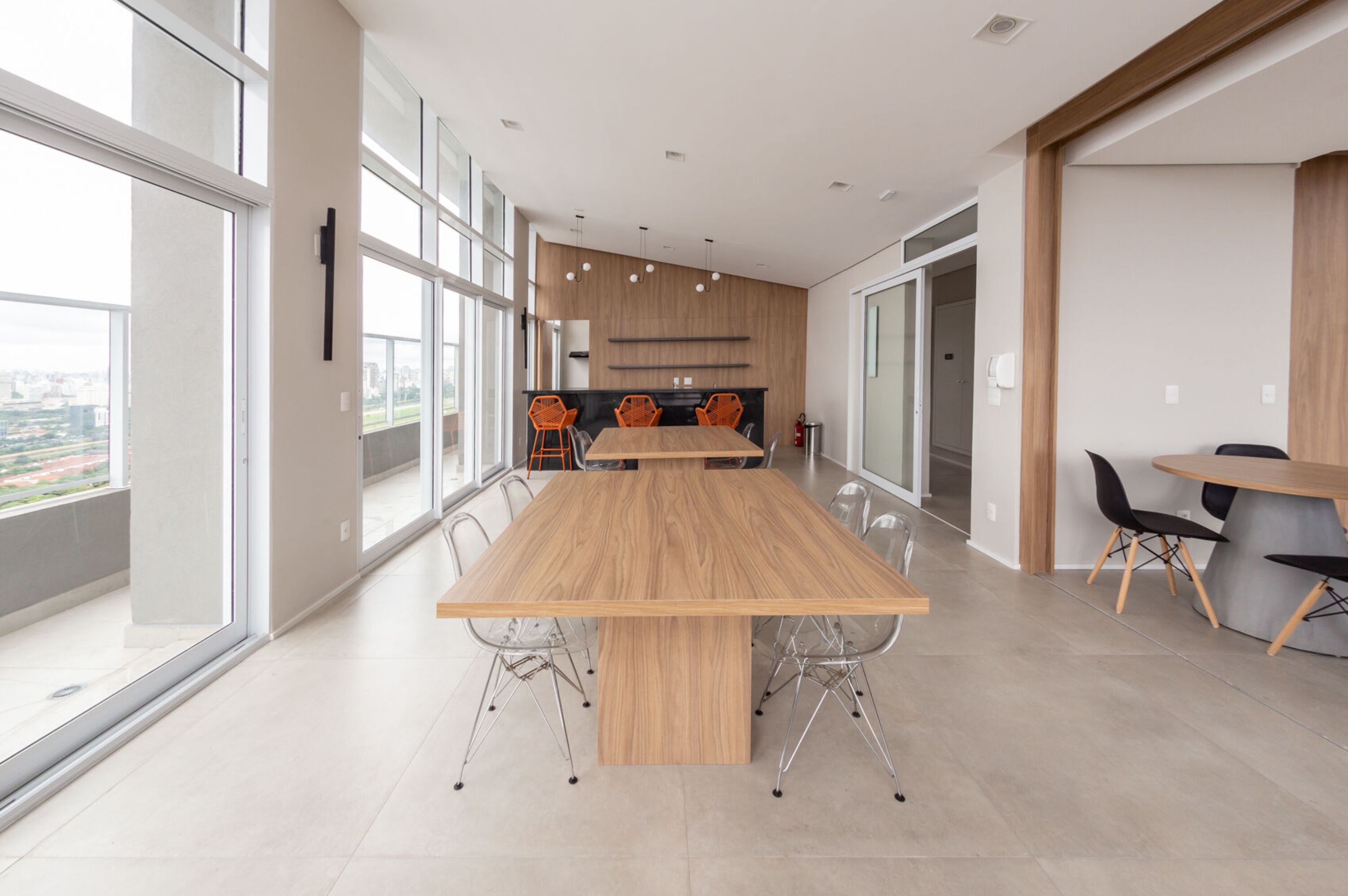 Una sala de conferencias moderna con una gran mesa de madera, paredes de vidrio transparente y vistas a la ciudad.