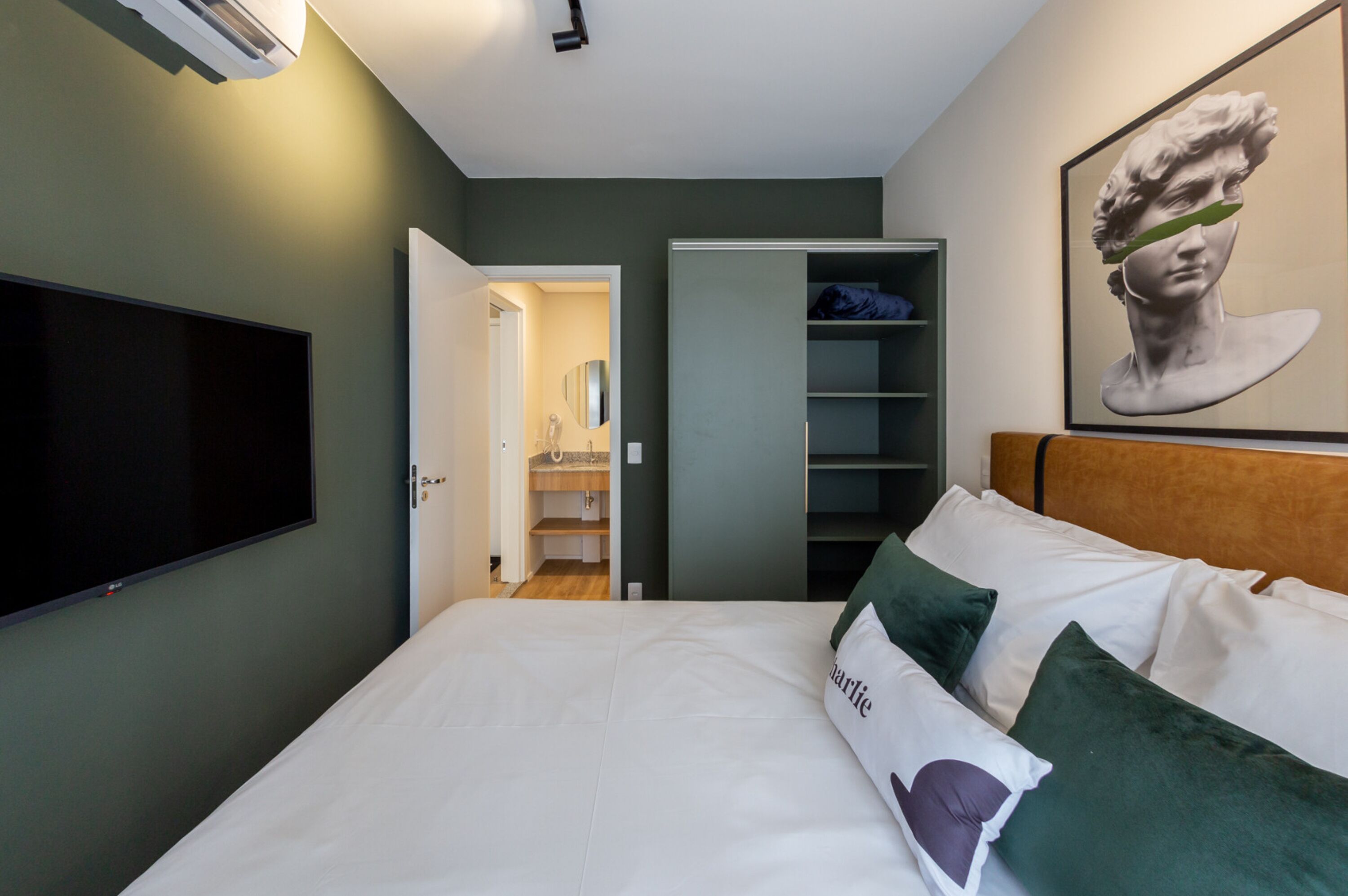 A bedroom with a bed, a television, a wardrobe, and a painting on the wall.